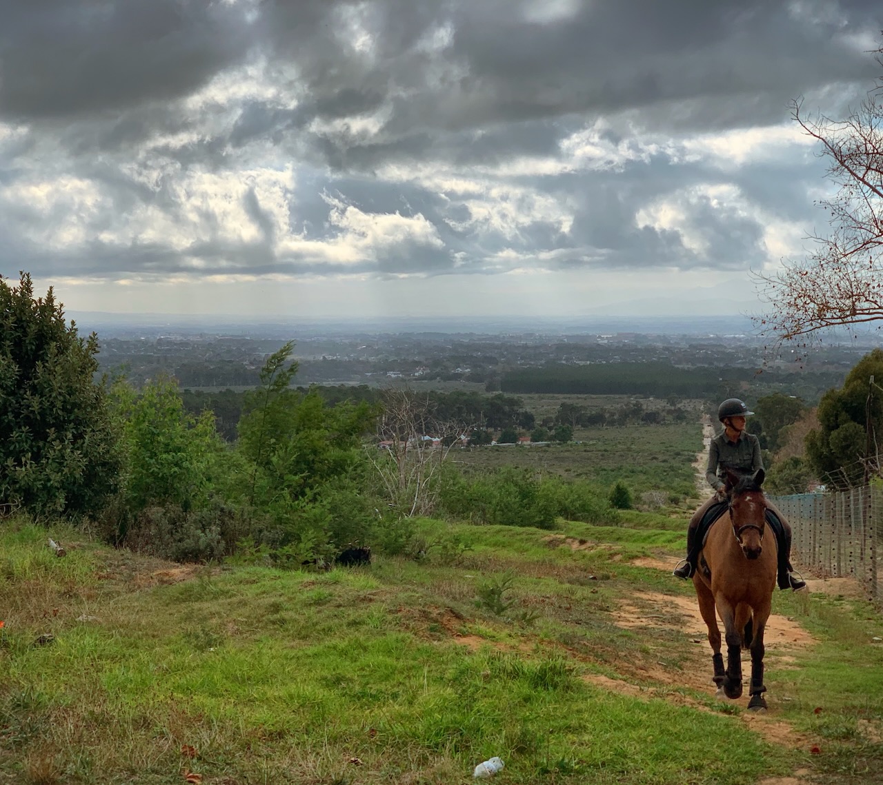 Rider on horseback with panoramic valley and city views under dramatic cloudy skies
